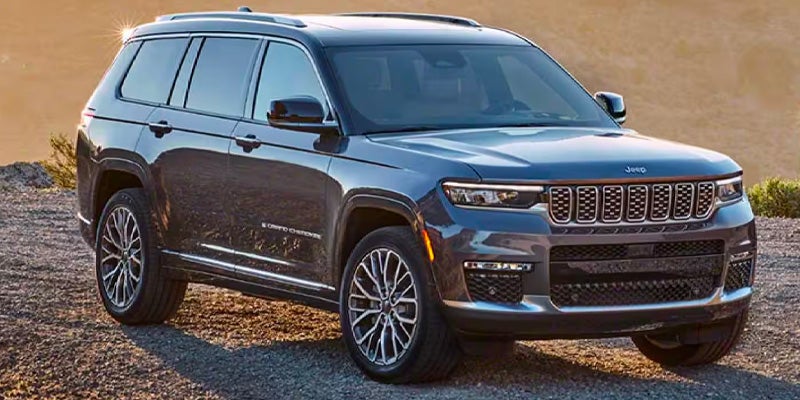 A dark gray 2022 Jeep Grand Cherokee L SUV with a seven-slot grille, parked on rough terrain during sunset.