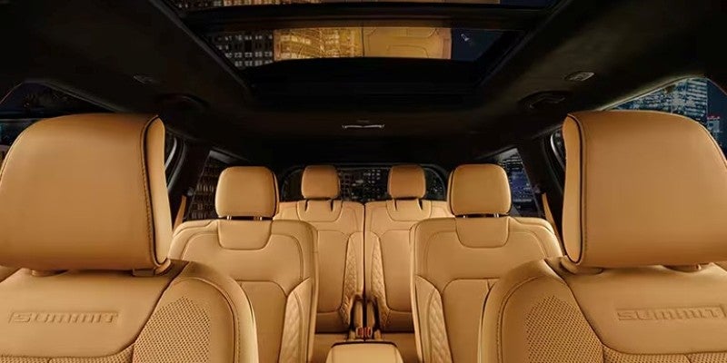 Interior of a luxury car with light-brown leather seats, a dark ceiling, and a panoramic sunroof.