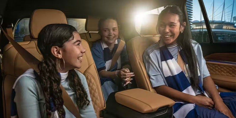 Three smiling young women in striped shirts and scarves, seated in the back of a luxury car.