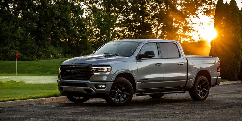 Gray Ram pickup truck parked on asphalt, green golf course and trees in background, sunset in top right.