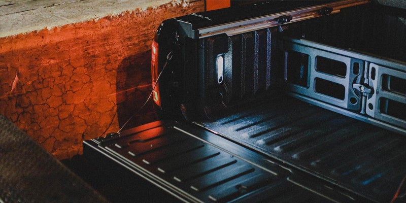 Truck bed with a black retractable tonneau cover, illuminated by a warm orange light.