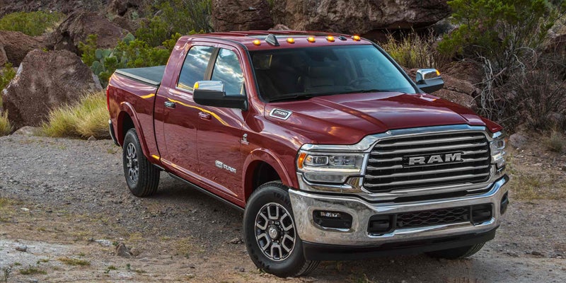 A red Ram pickup truck with a black bed cover, parked on a gravel path amidst desert rocks and greenery.