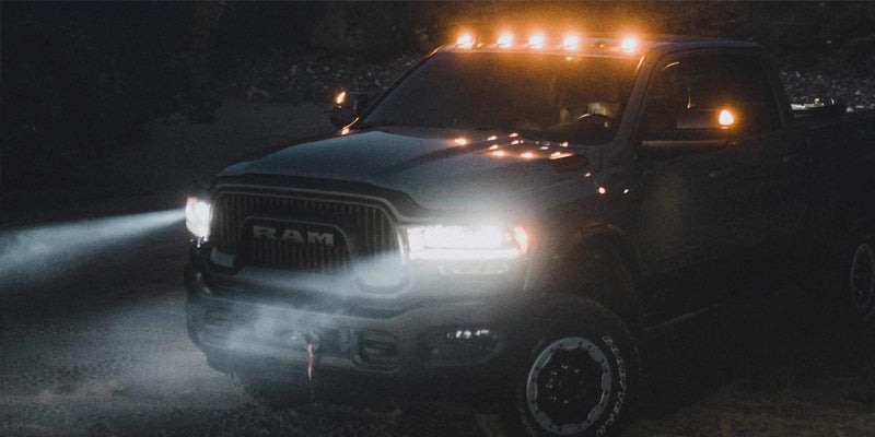 Dark Ram truck with bright headlights and amber roof lights driving at night.