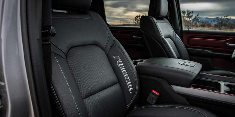 Close-up of a black leather car seat with "REBEL" embroidered in white, beside a center console.