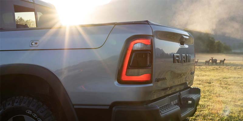 Rear of a gray Ram truck with illuminated tail light and embossed "RAM" logo, sunburst, and elk herd.