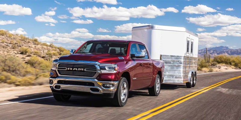 A red Ram pickup truck pulls a white and metal trailer along a desert highway.