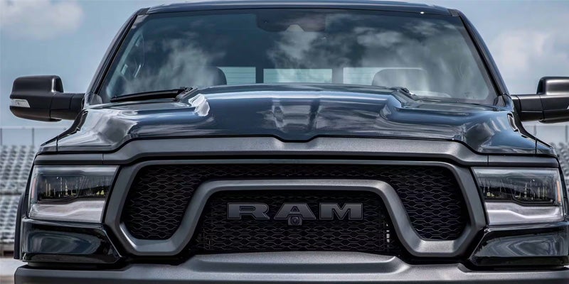 Front view of a dark gray Ram truck with the RAM logo on the grille, headlights shining brightly.