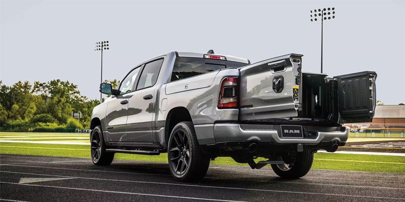 Rear view of a grey Ram 1500 truck with the multifunction tailgate open, showing two swing-away doors.