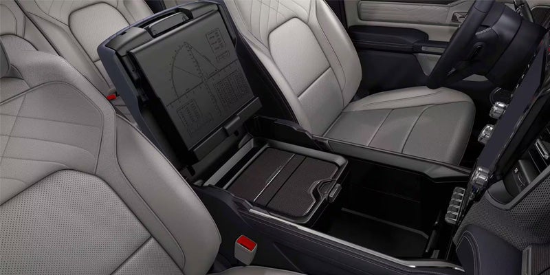 Open center console in a light gray leather car interior, revealing storage compartments and power conversion charts.
