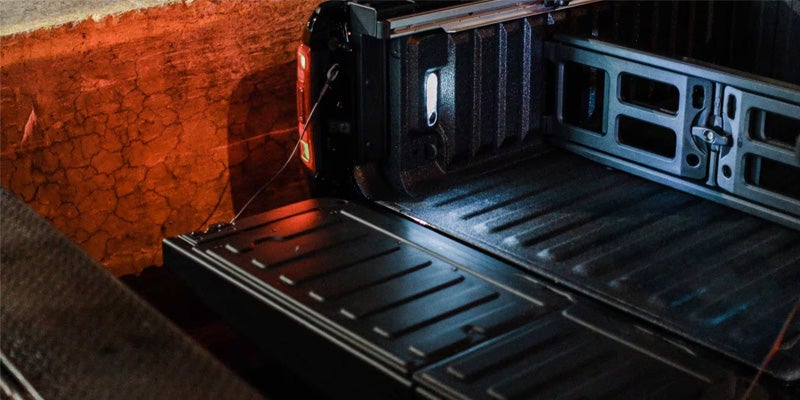Open, textured truck bed with tailgate lowered, illuminated by orange light.