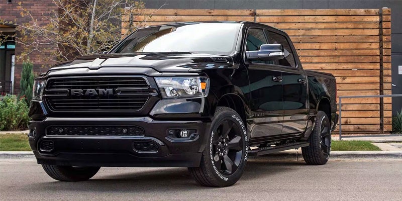 A black 2020 Ram 1500 pickup truck parked on asphalt with a modern wooden fence in the background.