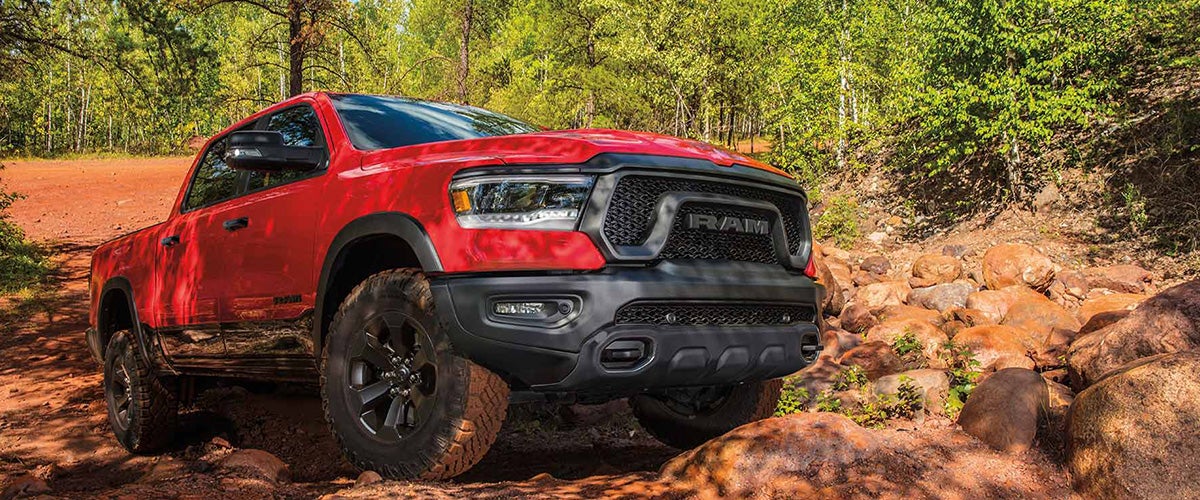 A bright red Ram truck with black accents, positioned on a rocky dirt path in a forest setting.