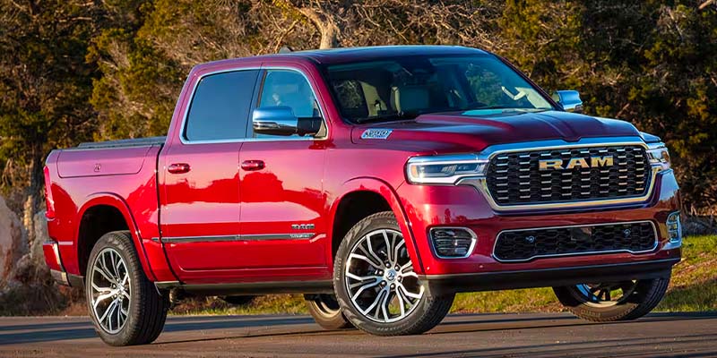 A red Ram pickup truck with chrome accents and large wheels parked on asphalt, trees in the background.