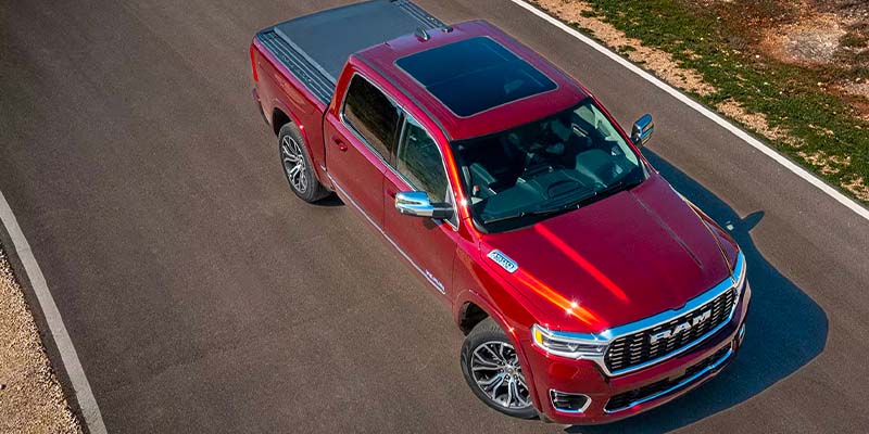 Overhead, a shiny red Ram pickup truck with a black sunroof and bed cover on an asphalt road.