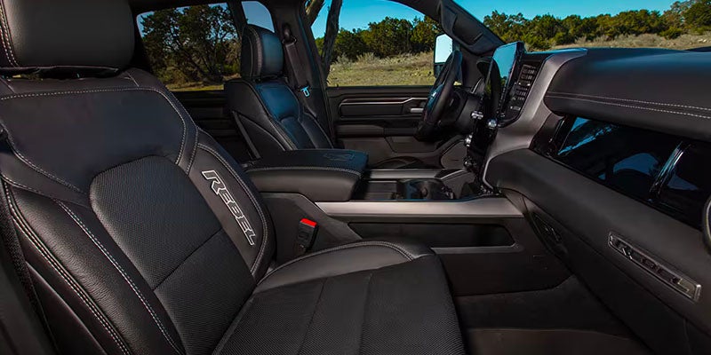 Interior of a Ram Rebel truck showing dark leather seats with white stitching and "REBEL" embroidered on the front seat.